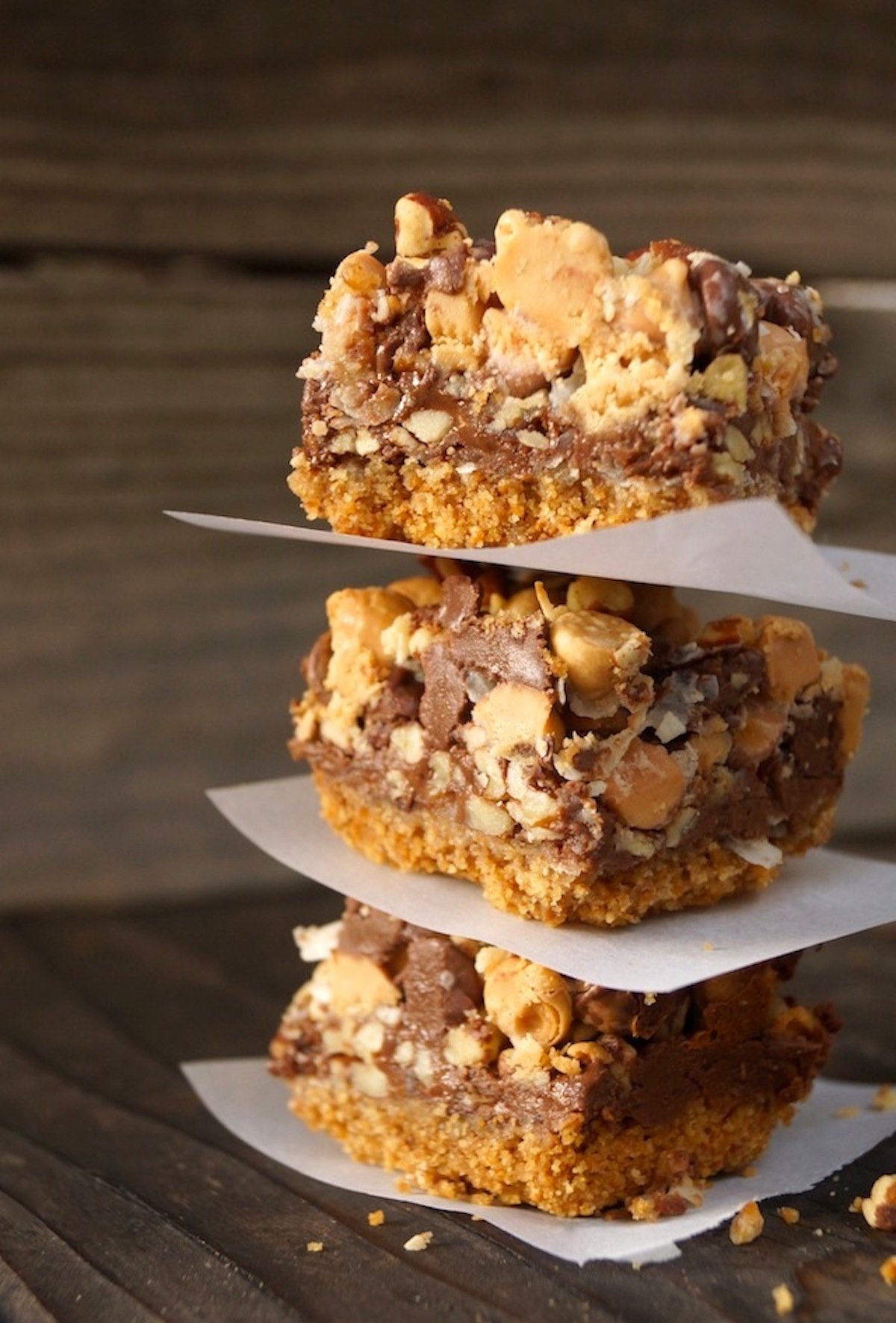 Three seven layer pretzel bars in a stack with parchment paper between each one.