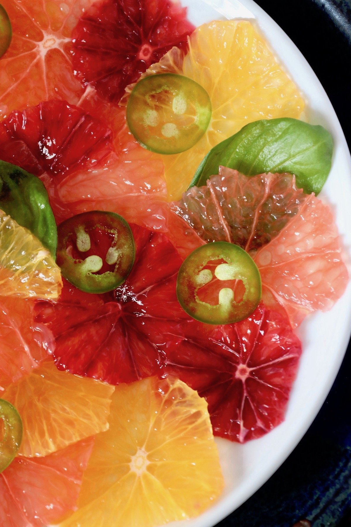 Close up of super thinly sliced citrus, pink, red and orange  on a white plate.