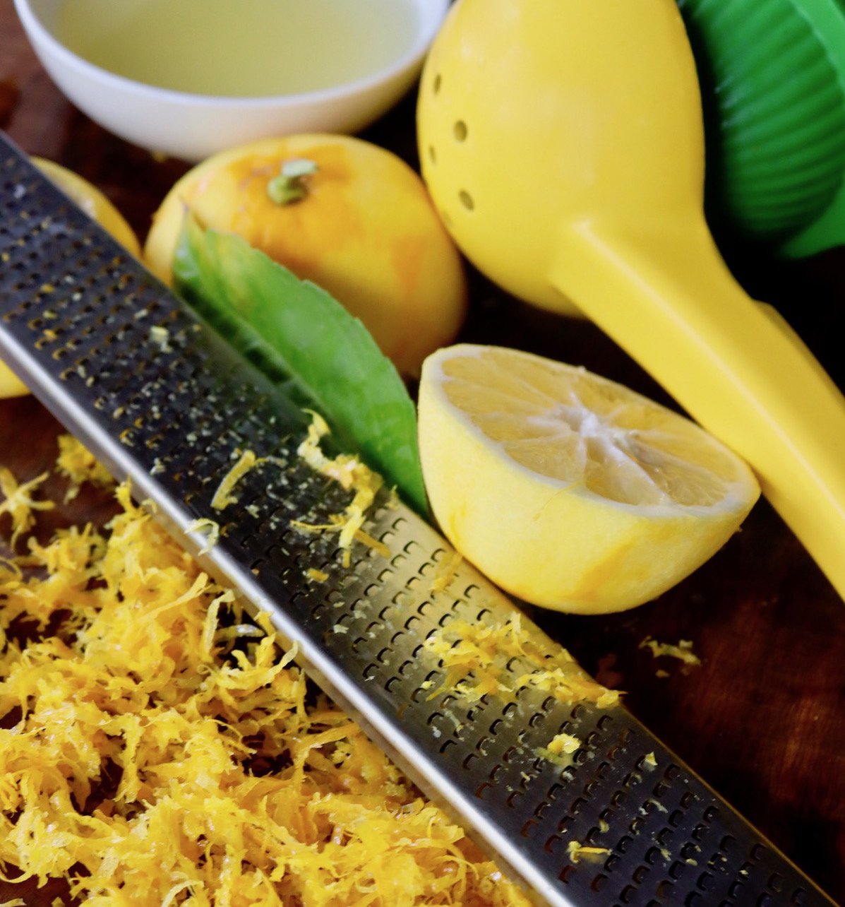 Zested lemon, lemon zester and pile of zest on cutting board.