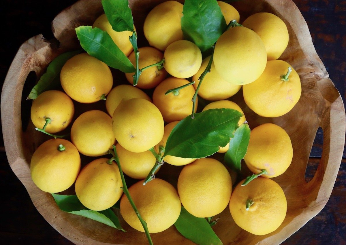 Wooden tray with a big pile of meyer lemons with their leaves.