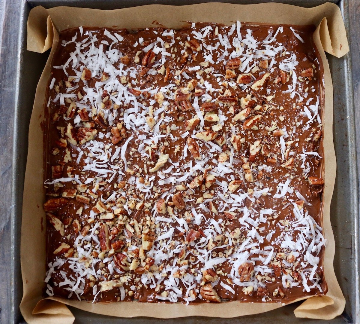 Chocolate coconut and pecan pieces in a parchment paper-lined square baking pan.