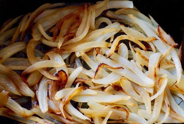 Sautéed onion slices in a black pan.