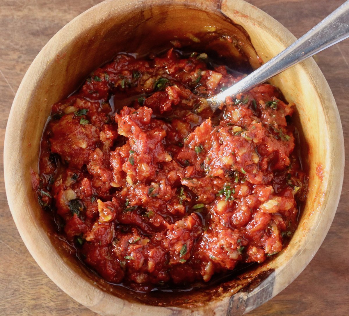 Small wooden bowl with paprika, fresh thyme leaves, lemon zest and tomato paste all mixed together with a spoon.