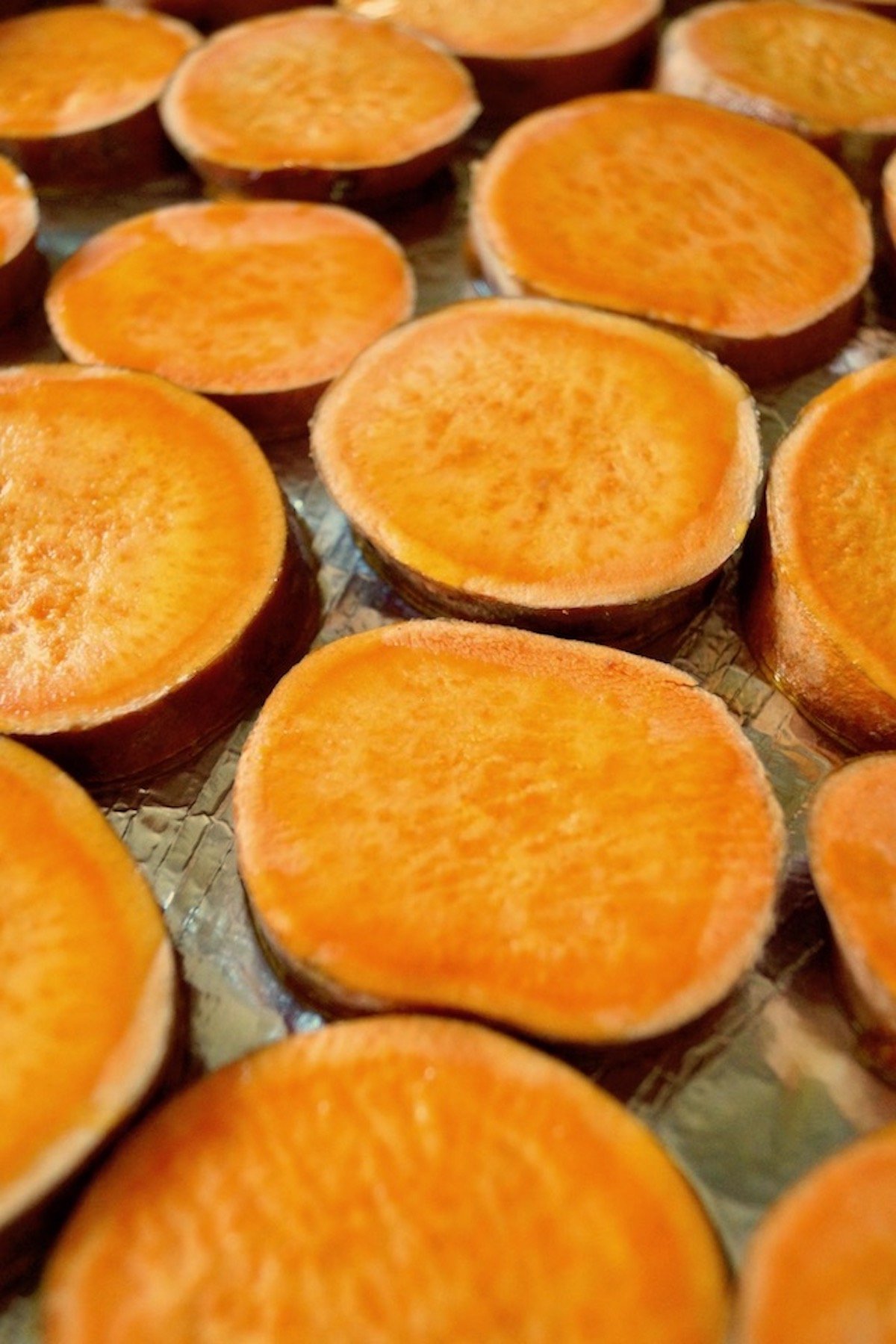 Several slices of sweet potatoes on a foil-lined baking sheet.