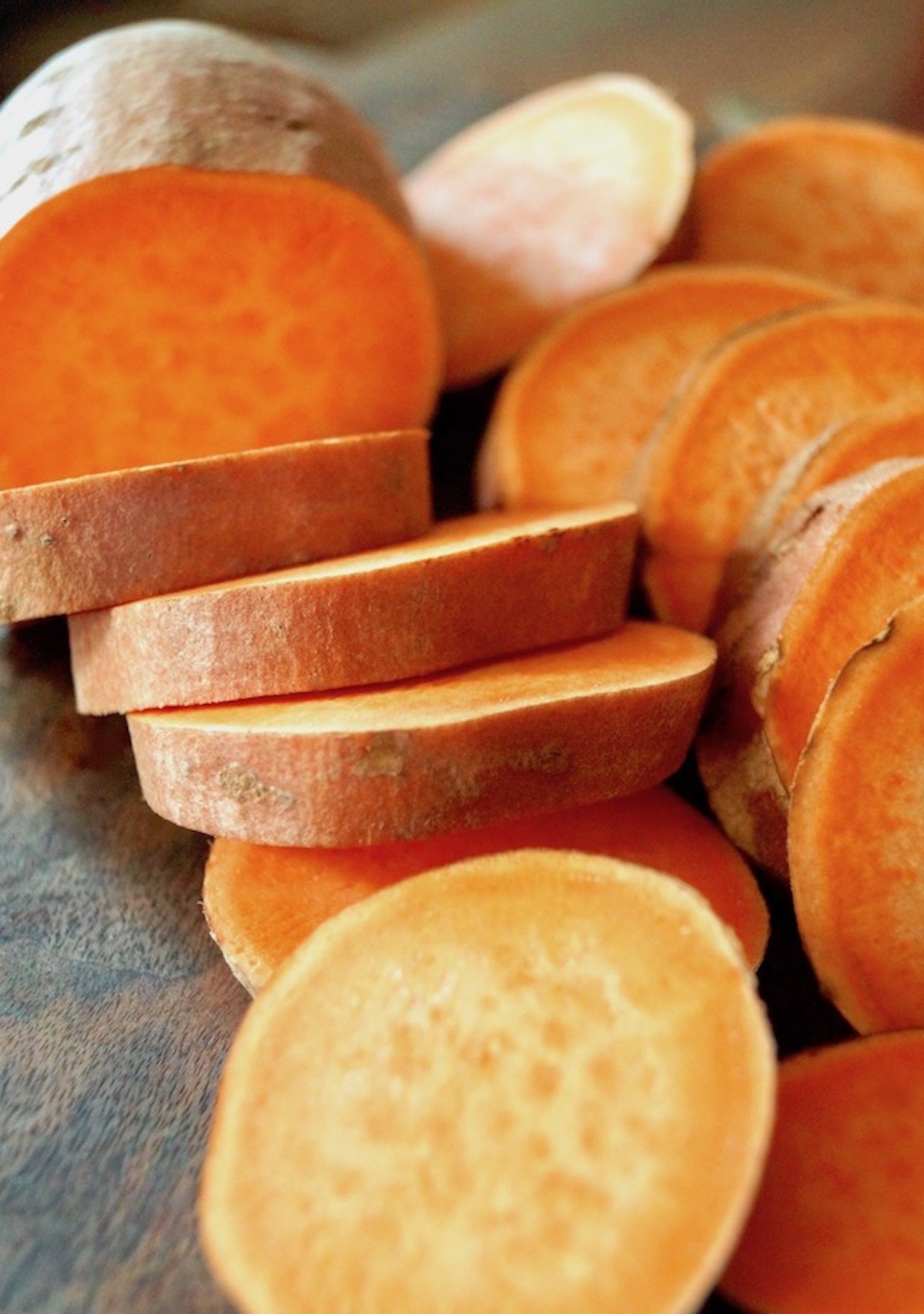 One large sweet potato on a cutting board, mostly cut into slices.