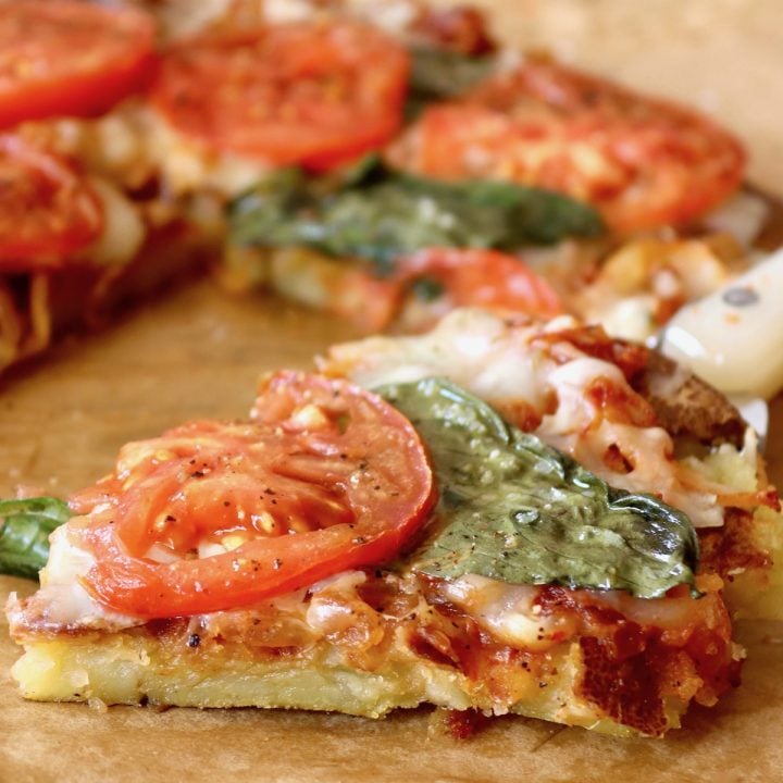 Small onion pizza with tomato slices on top with one slice being removed.