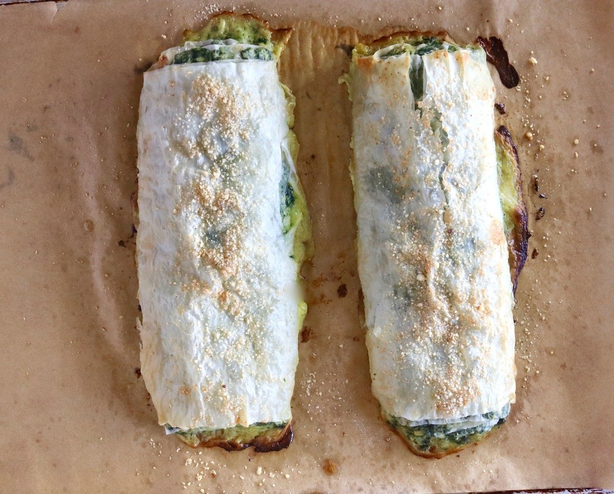 Two rolls of baked crispy phyllo dough with spinach filling on parchment paper.