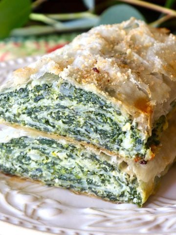 Two stacked Spinach and Ricotta Rolls on a cream-colored plate with Eucalyptus leaves behind it.