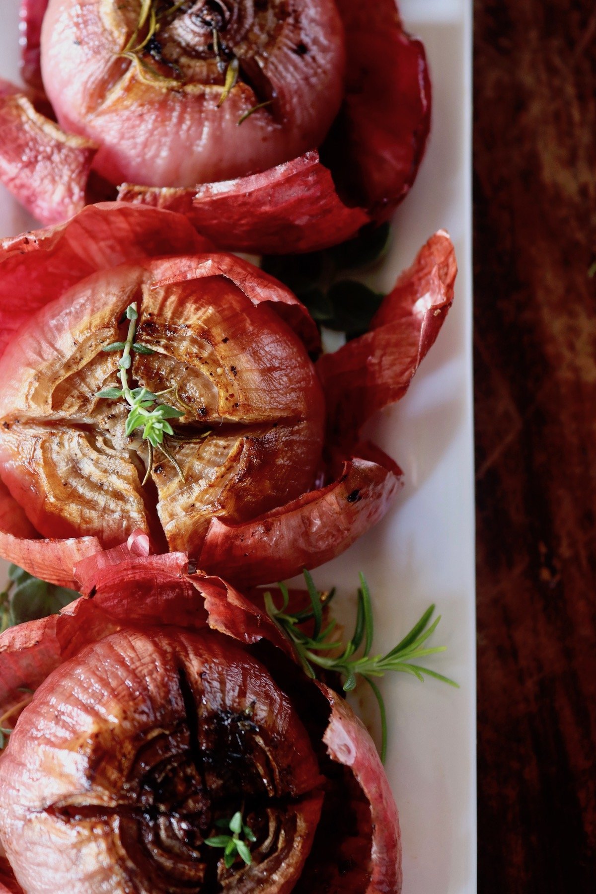 Three roasted red onions with their skins, on a white narrow plate.