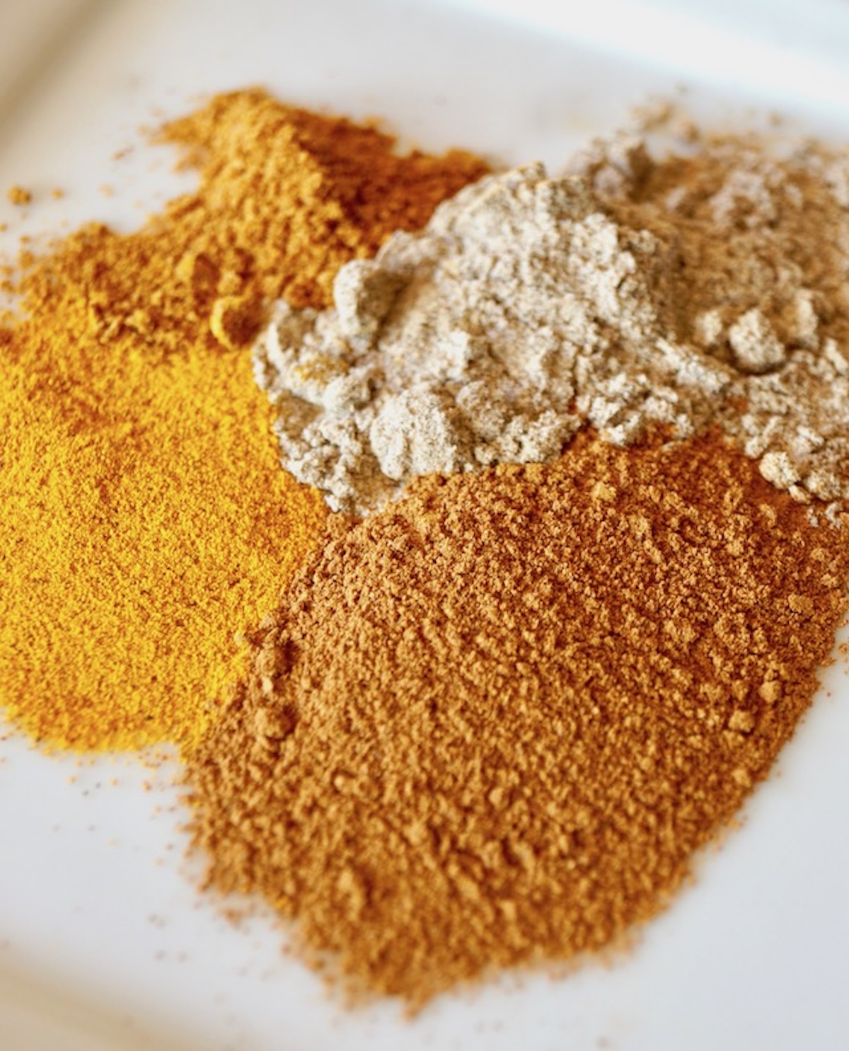 Warming spices o a plate including cardamom, cayenne, turmeric, and cinnamon.