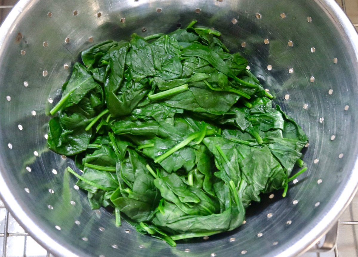 Colander in sink with cooked spinach leaves draining.