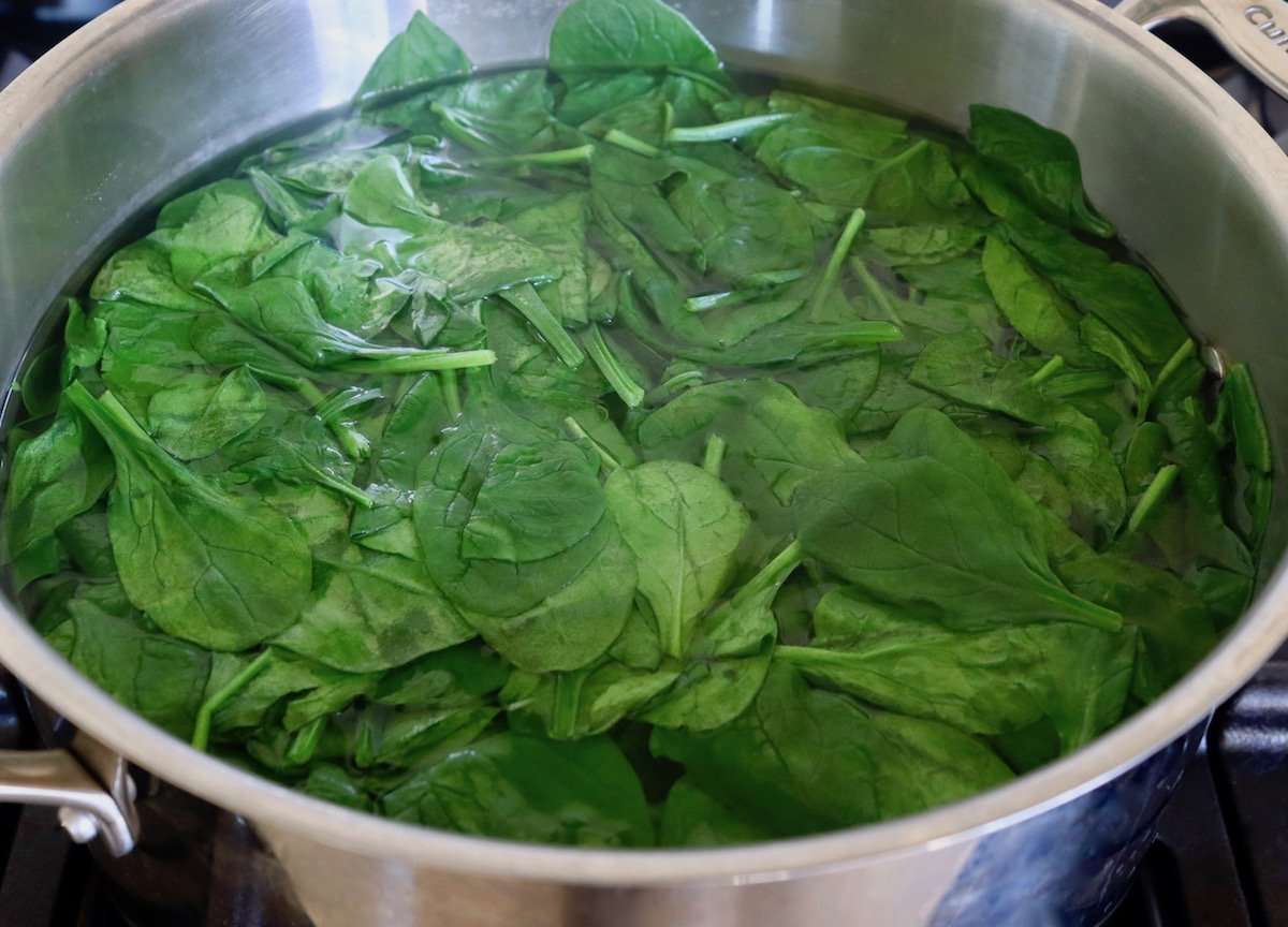 Large pot of hot water on the stove full of wilted spinach leaves.