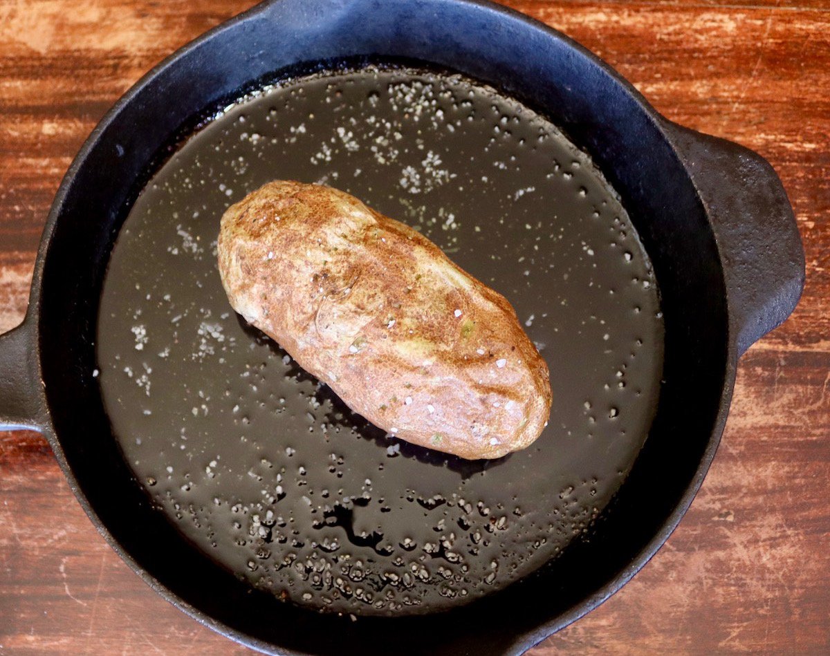 One whole baked potato in an oiled cast iron skillet.