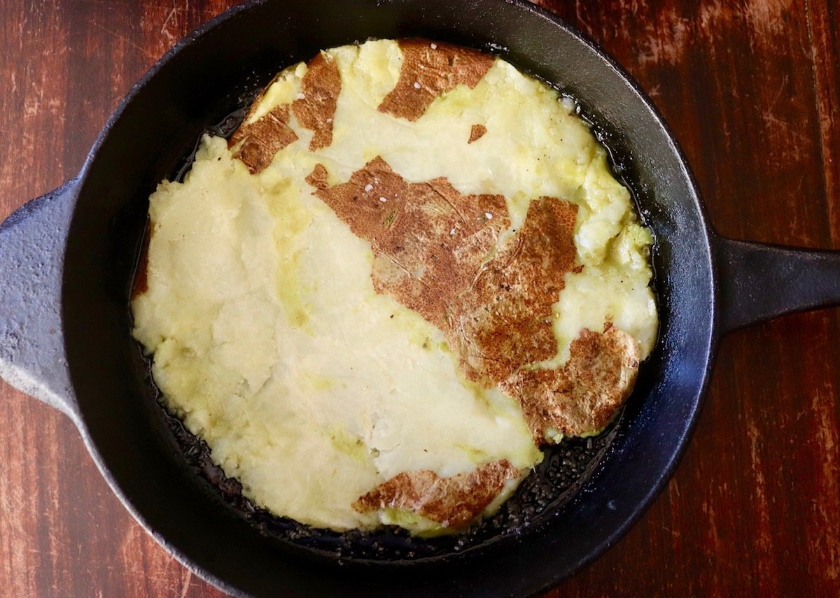 One large smashed Russet potato in a cast iron skillet.