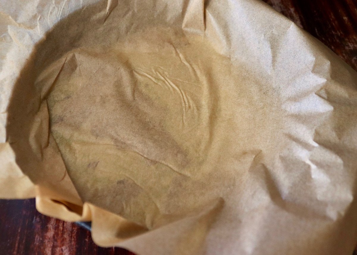 Skillet with a smashed potato under parchment paper.