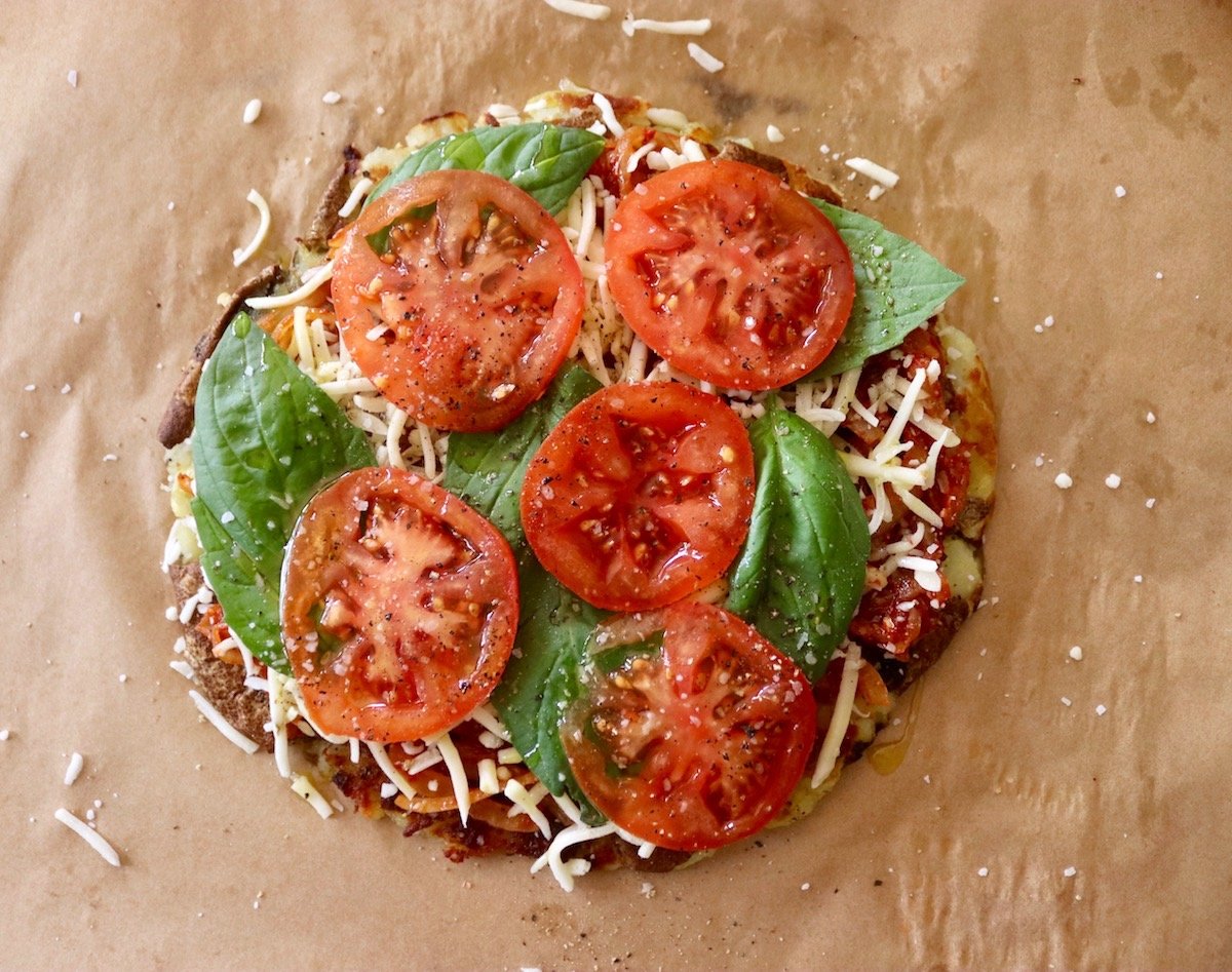 Potato pizza crust with basil leaves and sliced tomatoes.