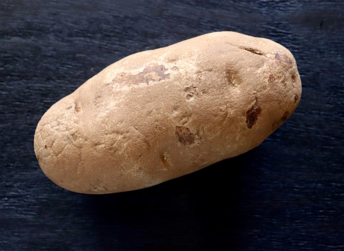 Large raw Russet potato on a black surface.