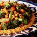 Big blue and white ceramic plate with Charred broccoli on top of red-orange sauce and topped with garbanzo beans and tomato slices.