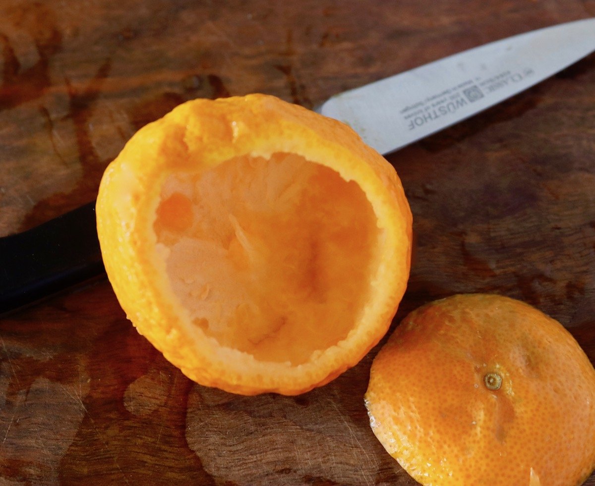 Empty tangerine peel that looks like a bowl, on a dark wood cutting board.