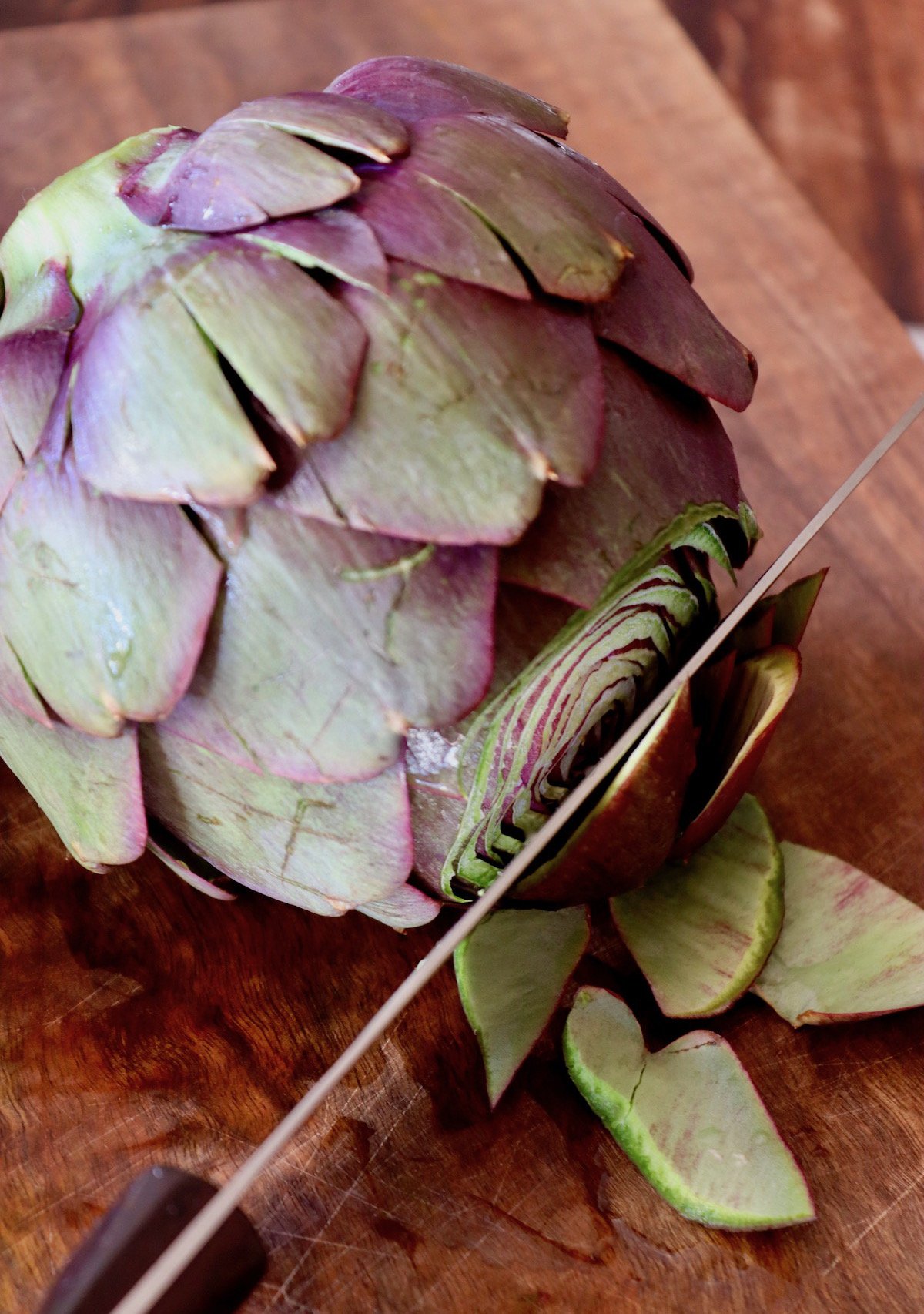 Purple artichoke with top inches being cut off.