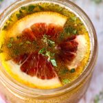Top view of a rounded jar with blood orange vinaigrette with a sprig of thyme on top.
