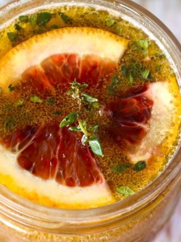 Top view of a rounded jar with blood orange vinaigrette with a sprig of thyme on top.