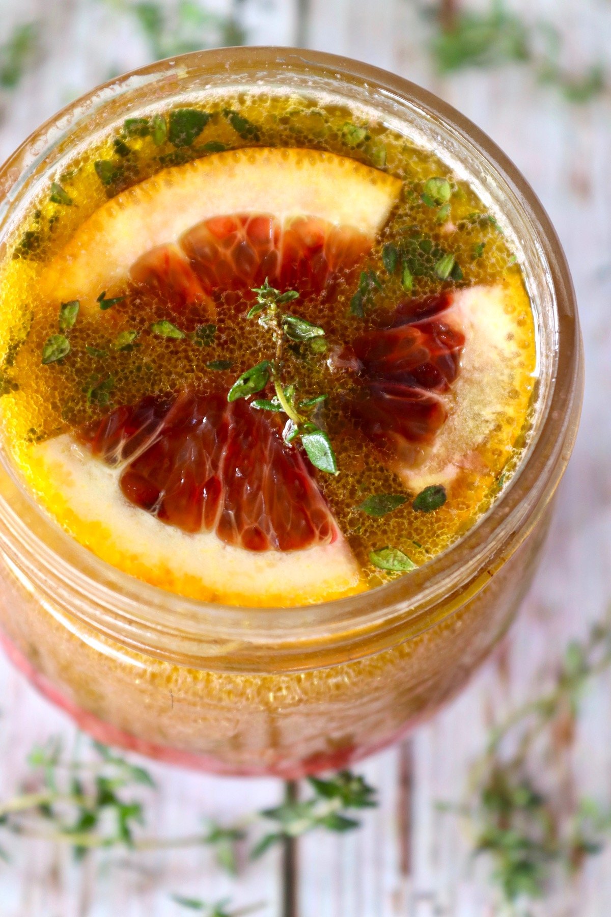 Top view of a rounded jar with blood orange vinaigrette with a sprig of thyme on top.