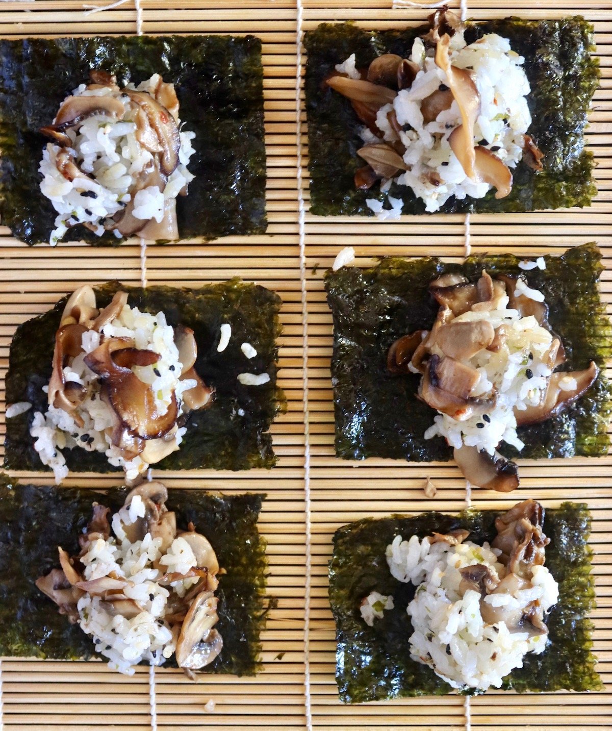 6 snack-sized Nori sheets on a sushi mat with rice-mushroom casserole scooped on top.