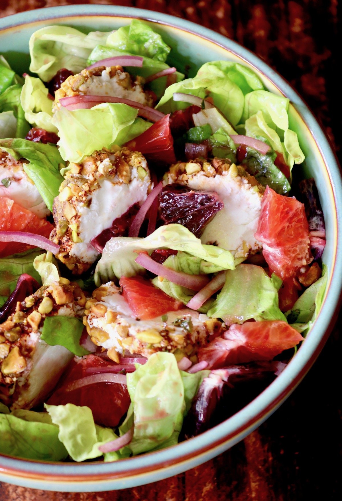 Top view of light green bowl filled with a vibrantly-colored goat cheese salad with blood oranges.