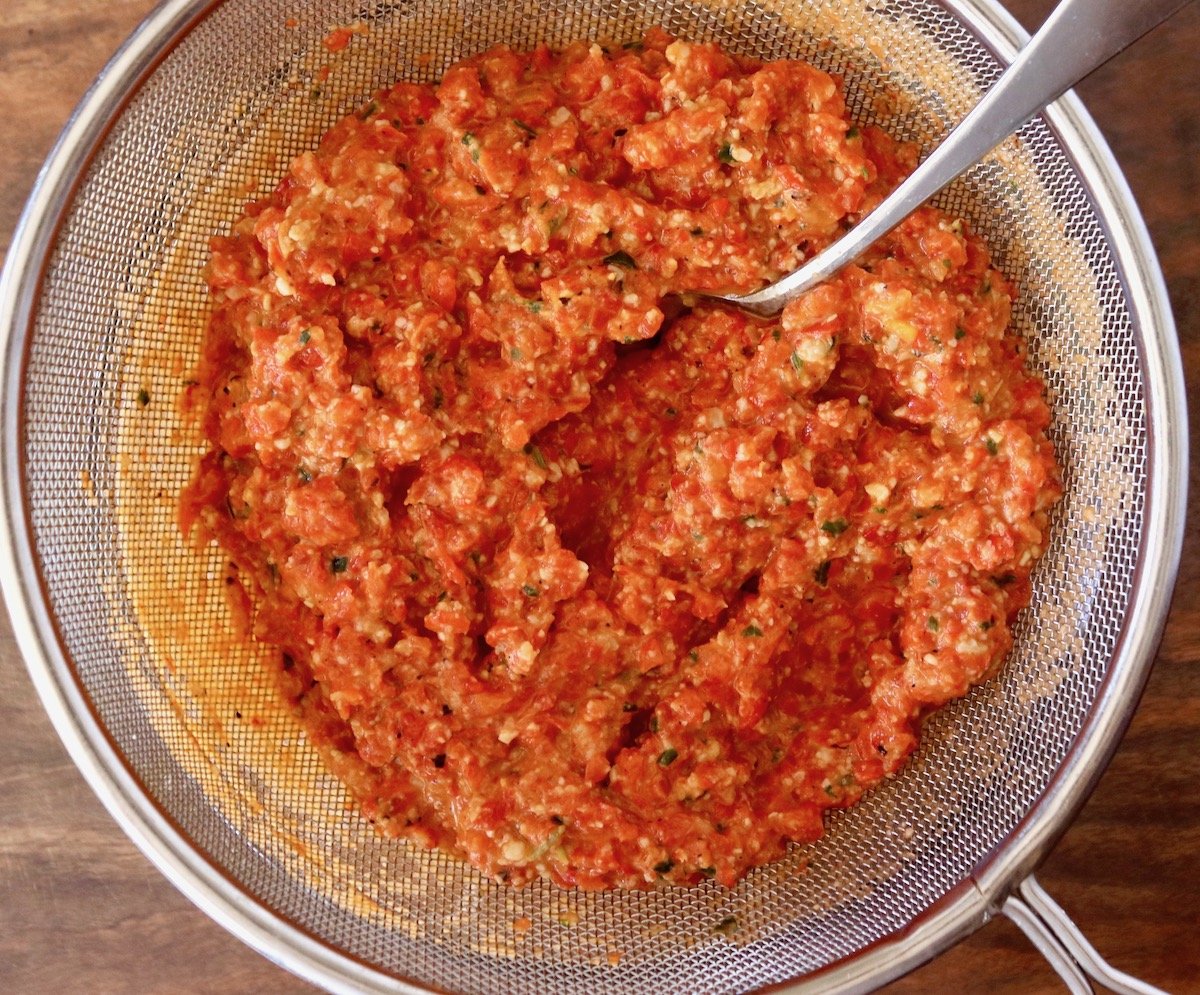 Red pepper pesto in a fine mesh strainer with metal handle.