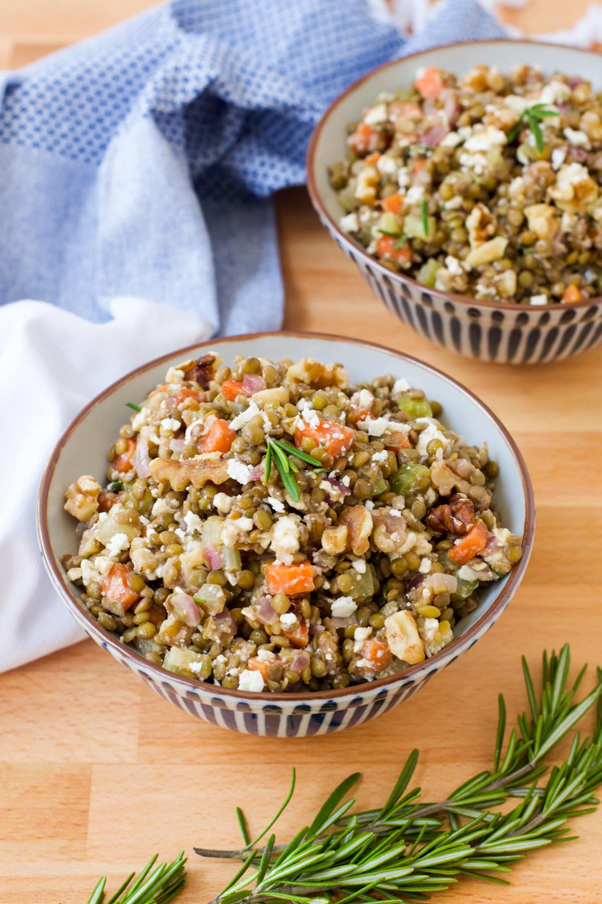 Lentil salad in round blue and white dish with chopped carrots and fresh sprig of rosemary.