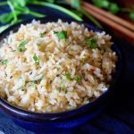 Miso rice in a dark blue bowl with wooden chopsticks in the background and fresh cilantro sprigs.
