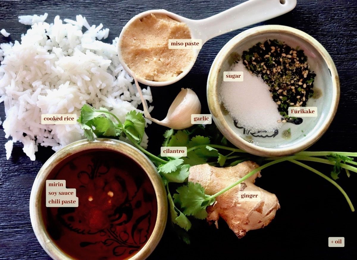Ingredients for miso fried rice on black cutting board, including cooked rice, miso paste, sugar, Furikakte, ginger, cilantro, garlic and chili paste.