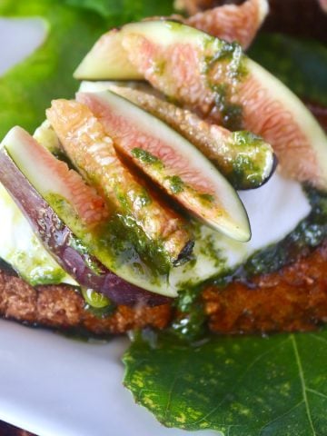 Close up of fig toast on dark bread on top of a fig leaf on a white plate.