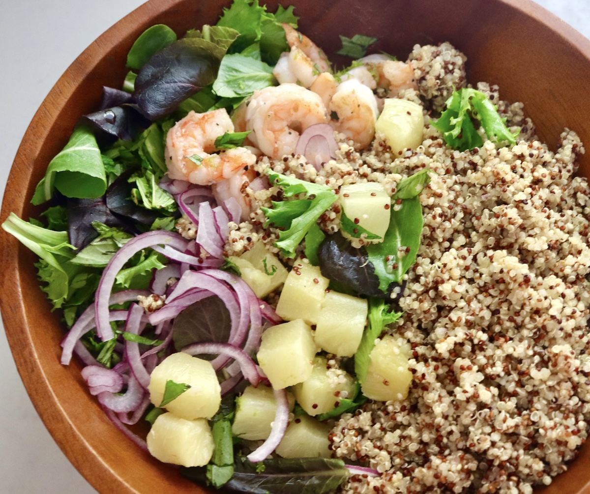 Large wooden salad bowl with quinoa, cooked shrimp, sliced red onion, lettuce and fresh herbs.