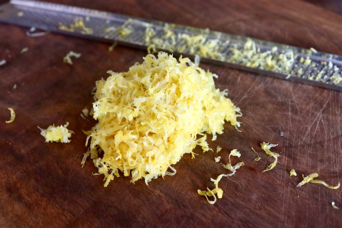 Small pile of lemon zest on a wooden cutting board with a microplane zester beside it.