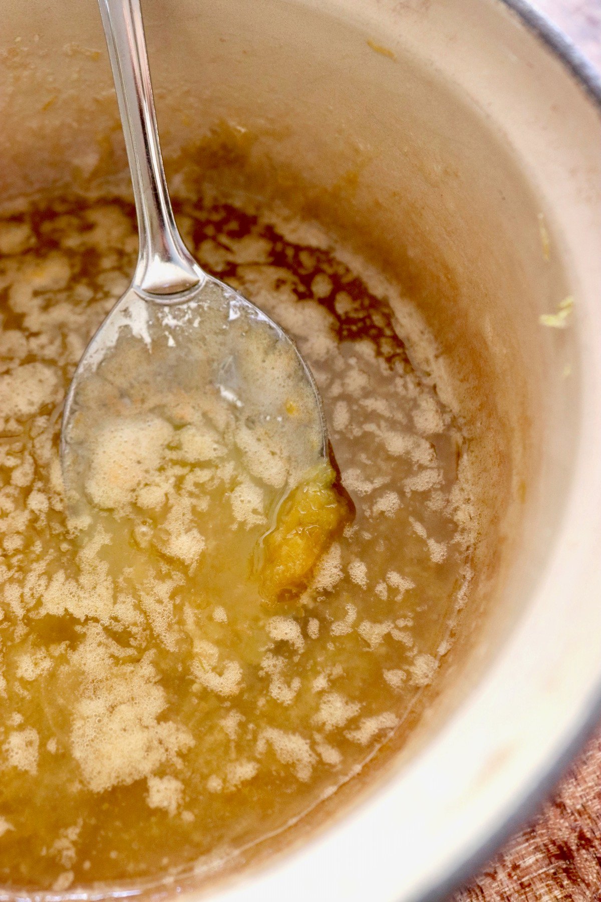 Melted butter with lemon zest and a mixing spoon in a cream-colored pot.