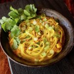Black ceramic bowl filled with curry udon and fresh cilantro sprigs.