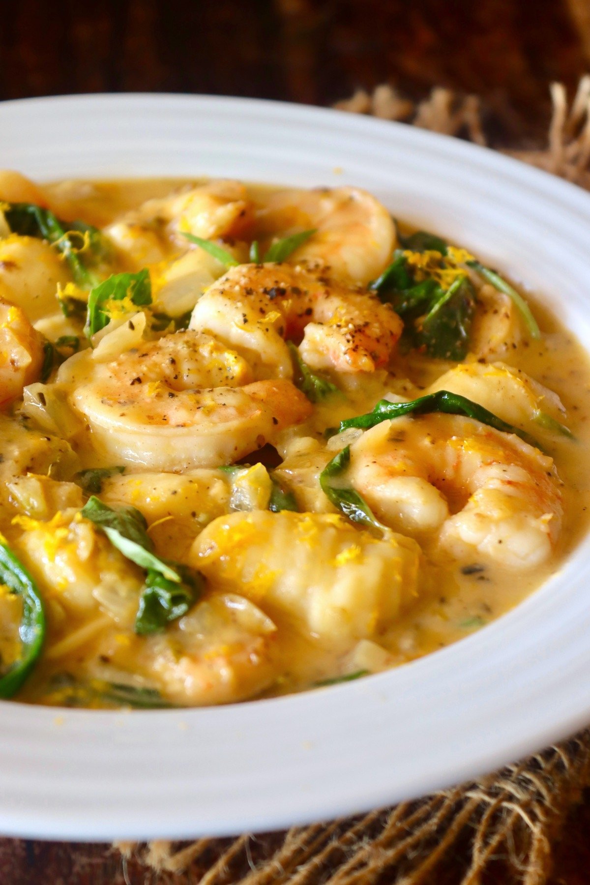 White shallow bowl filled with creamy coconut shrimp and spinach.