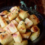 Roasted cubes of parsnips in a black bowl with a few sprigs of fresh thyme.