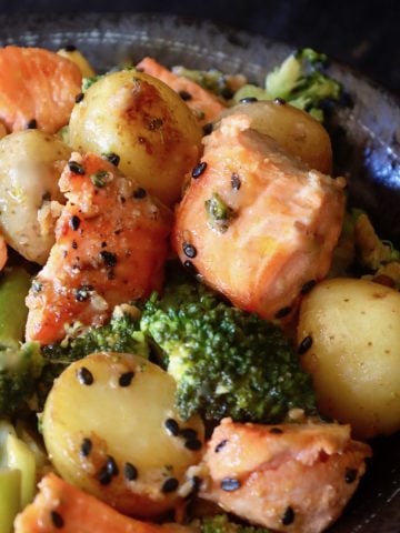 Top view of a black ceramic bowl filled with salmon, broccoli and tiny potatoes.