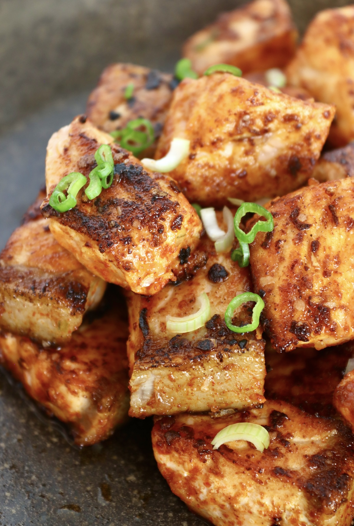 Small pile of crispy salmon bites on a black plate with diced scallions for garnish.