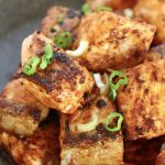 Small pile of crispy salmon bites on a black plate with diced scallions for garnish.