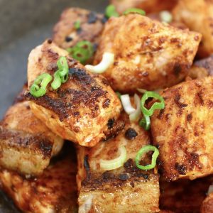 Small pile of crispy salmon bites on a black plate with diced scallions for garnish.