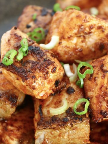 Small pile of crispy salmon bites on a black plate with diced scallions for garnish.