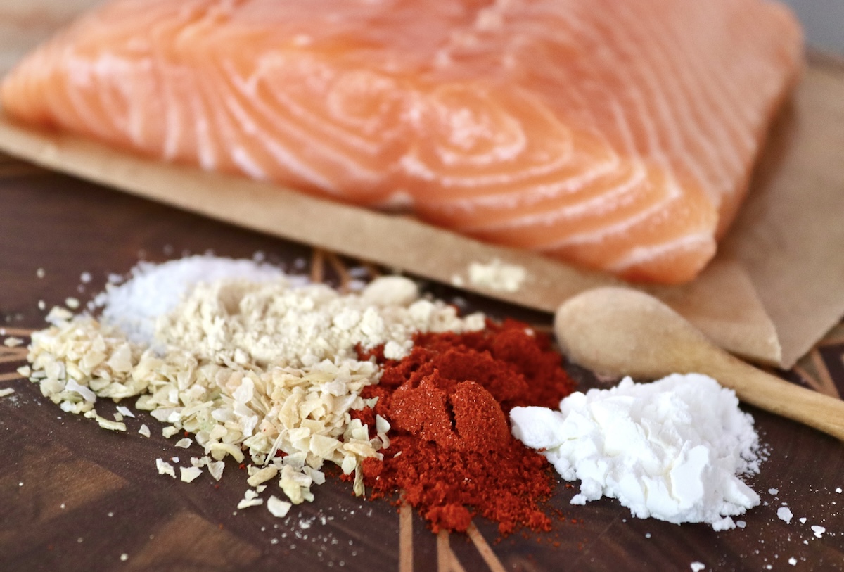 Stovetop-Crispy-Salmon-Bites Raw salmon fillet on parchment paper with little piles of salt, dried minced onion, paprika and cornstarch.