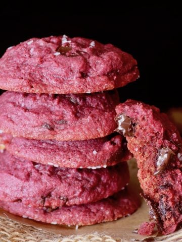 Stack of 5 magenta chocolate chip beet cookies with one broken in half leaning on the stack.