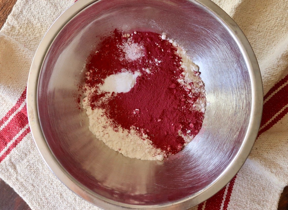 Stainless steel mixing bowl with flour and beet powder on top.