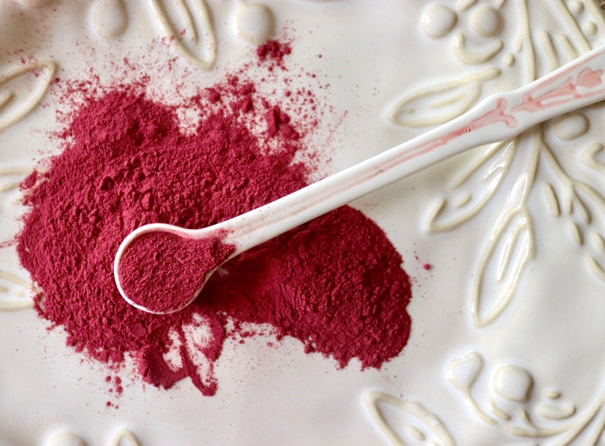 Beet root powder on a white spoon on a white plate with it spilling over.