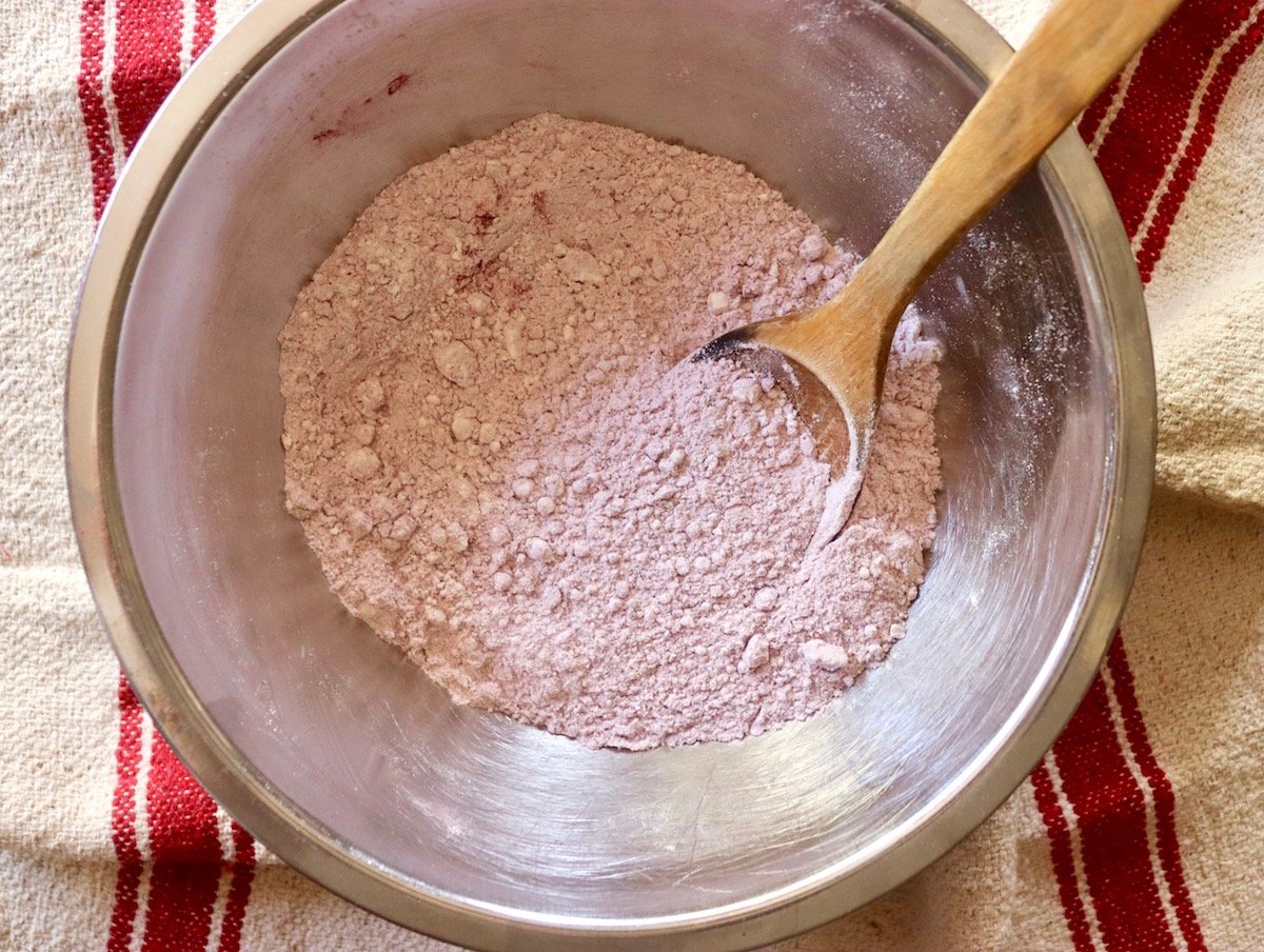 Stainless steel mixing bowl with flour and beet powder mixed together with a wooden spoon.